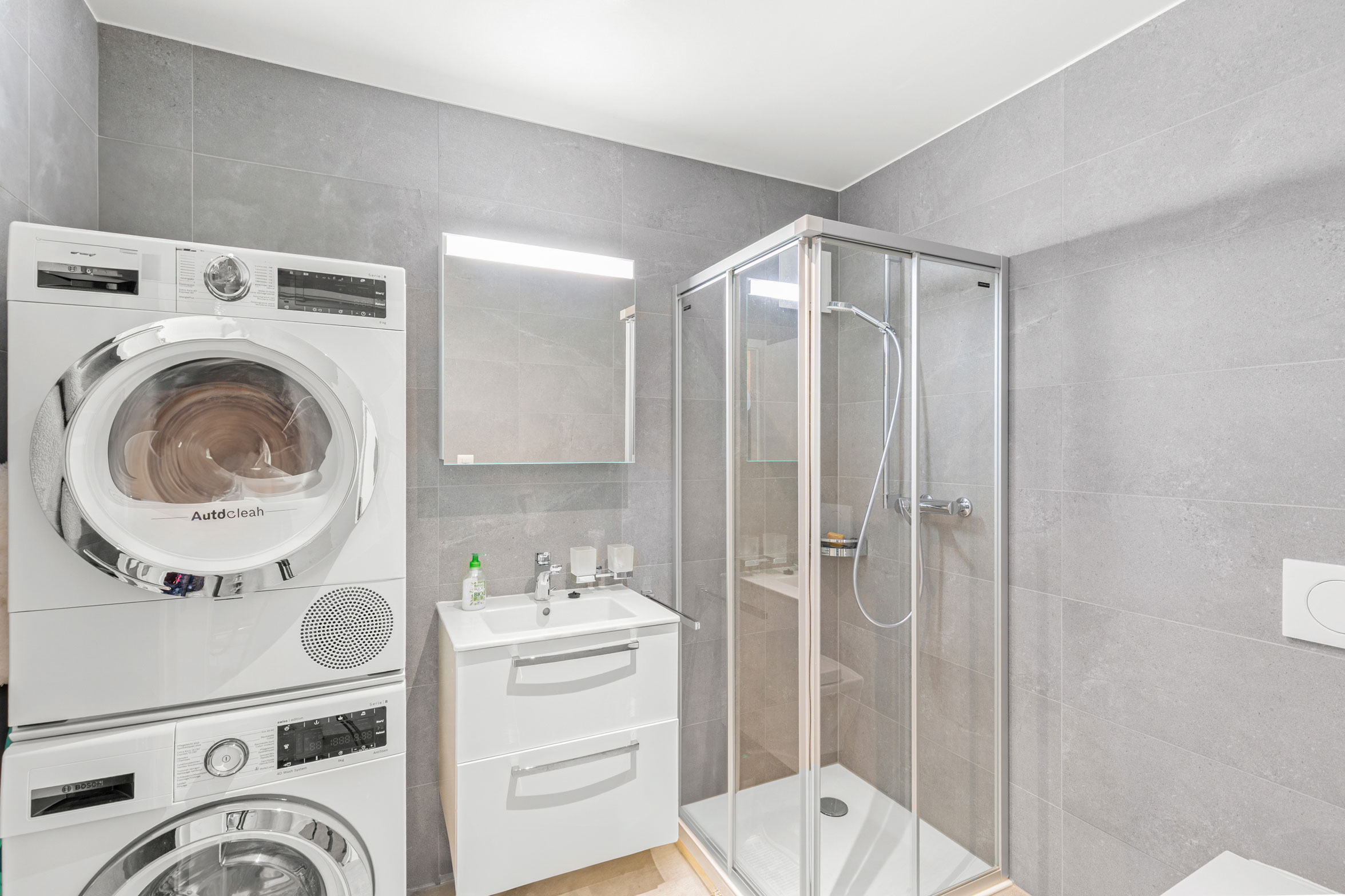 Salle d’eau avec douche vitrée, colonne de lavage et carrelage gris moderne