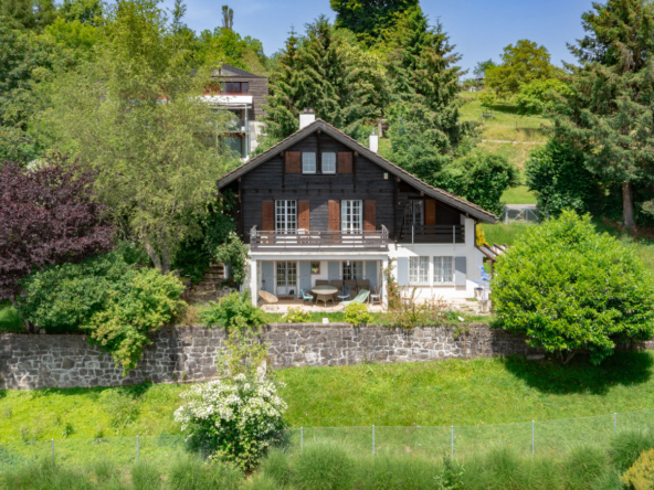 Façade d’un chalet traditionnel entouré de verdure à Jongny, avec terrasse et volets en bois