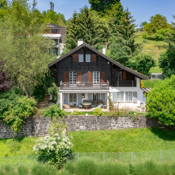 Façade d’un chalet traditionnel entouré de verdure à Jongny, avec terrasse et volets en bois