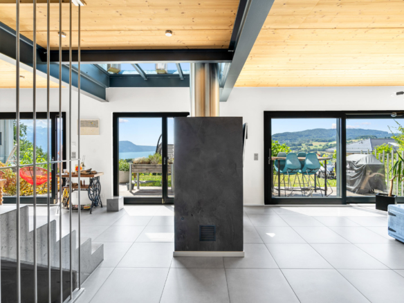 Vue intérieure lumineuse d’un salon contemporain avec baies vitrées ouvertes sur terrasse et paysage alpin à St-Légier