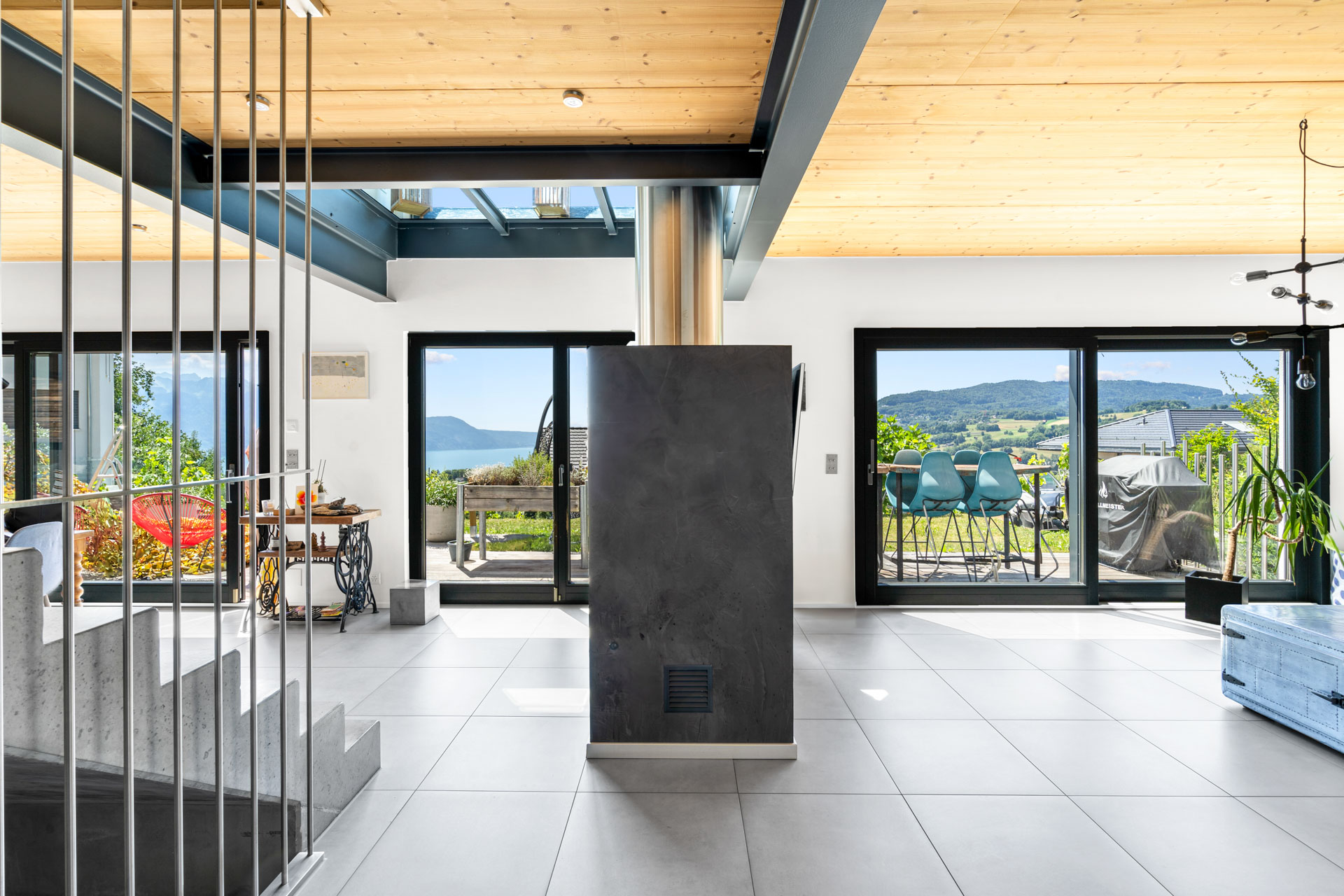 Vue intérieure lumineuse d’un salon contemporain avec baies vitrées ouvertes sur terrasse et paysage alpin à St-Légier