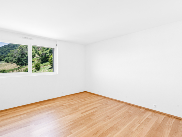 Chambre vide avec parquet clair et vue dégagée sur les collines verdoyantes