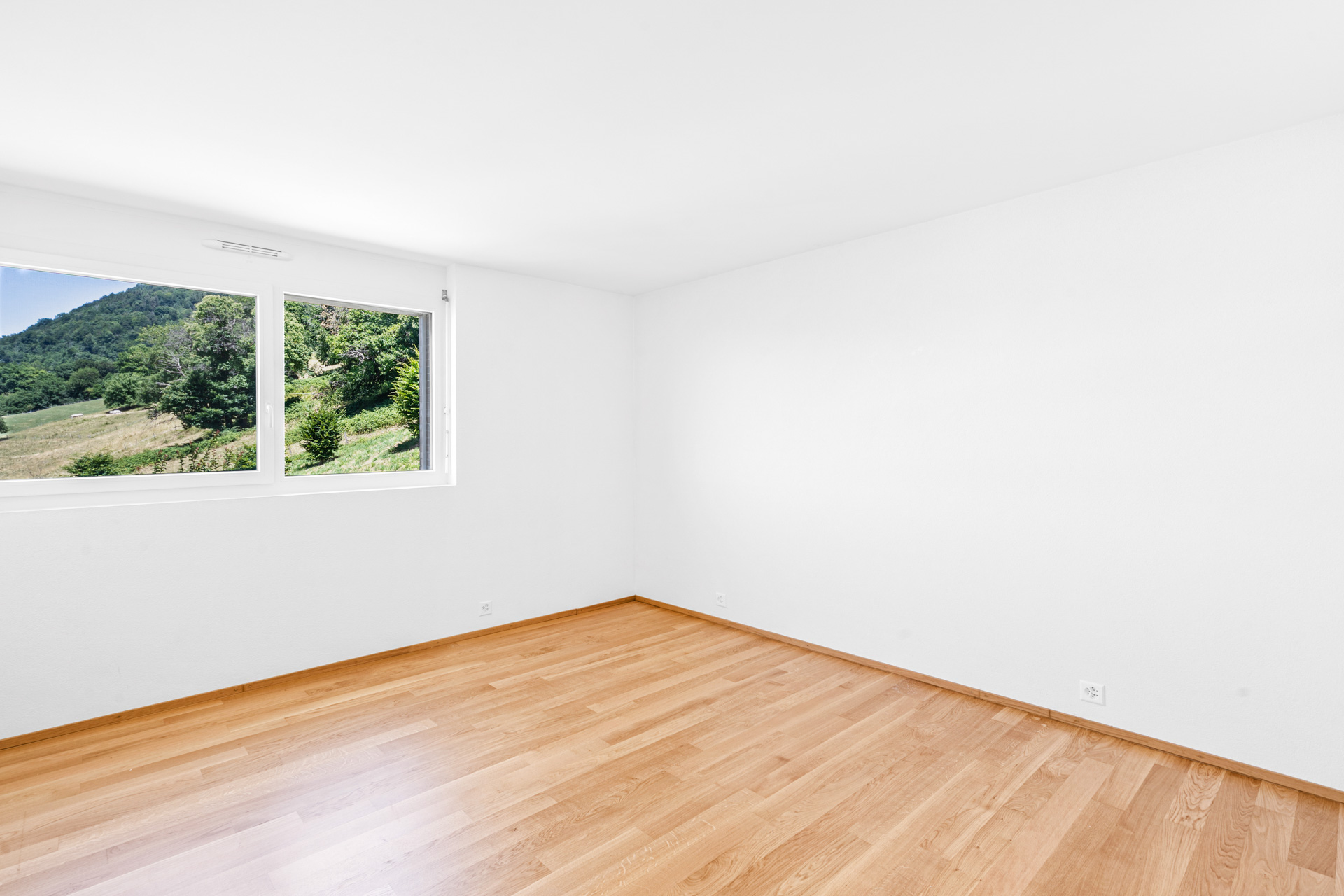 Chambre vide avec parquet clair et vue dégagée sur les collines verdoyantes