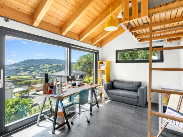 Bureau avec grande baie vitrée, mobilier en bois et vue dégagée sur les collines de St-Légier