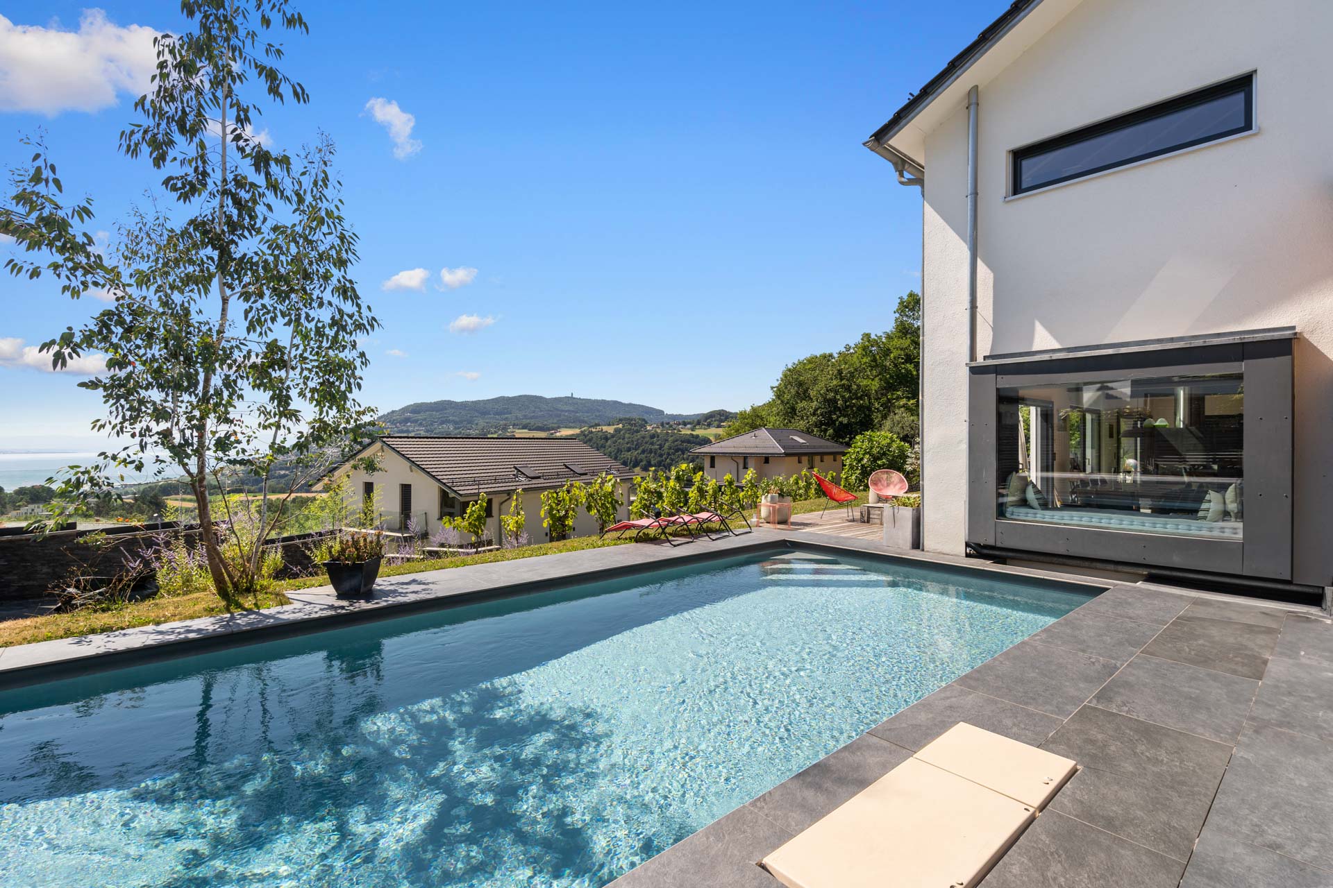 Piscine extérieure avec margelles sombres et vue sur le lac et les montagnes à St-Légier