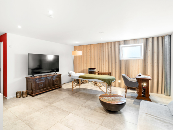 Salle multifonction aménagée avec table de massage, TV et mobilier en bois à St-Légier