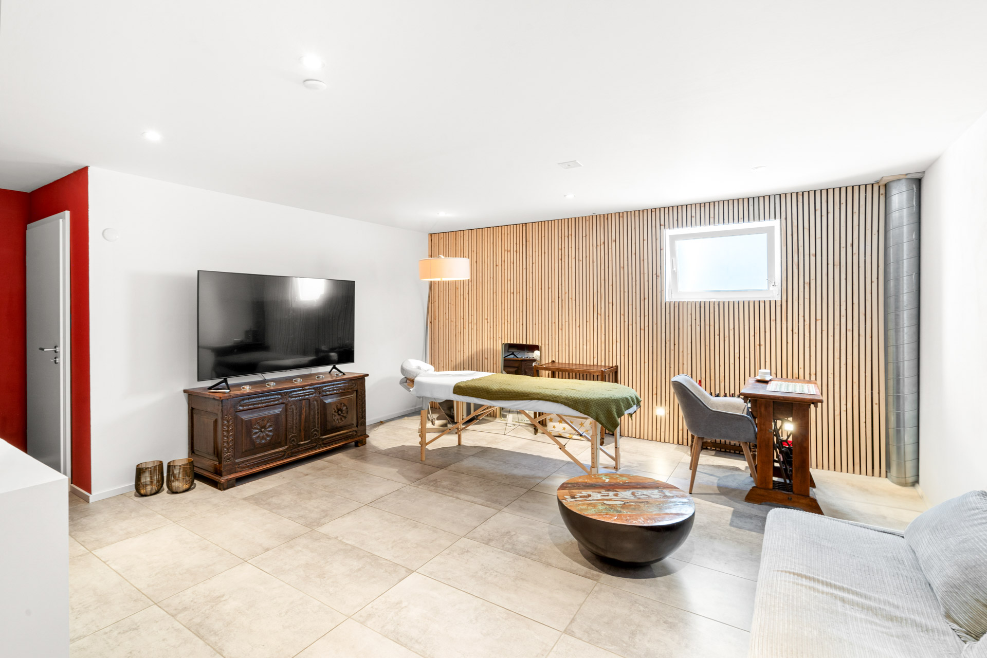 Salle multifonction aménagée avec table de massage, TV et mobilier en bois à St-Légier