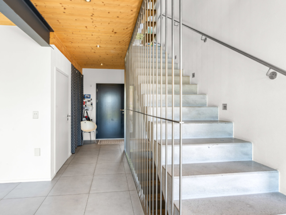 Escalier moderne en béton avec rambarde métallique, donnant sur un hall d’entrée épuré à St-Légier