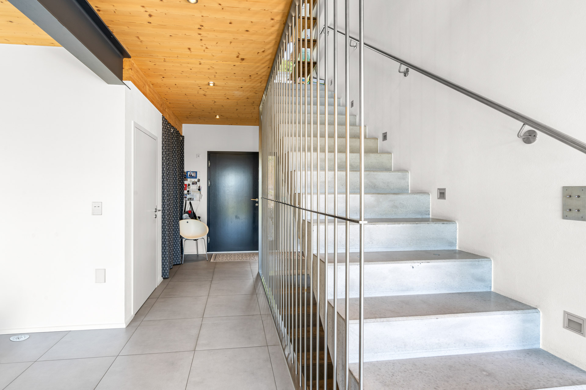 Escalier moderne en béton avec rambarde métallique, donnant sur un hall d’entrée épuré à St-Légier