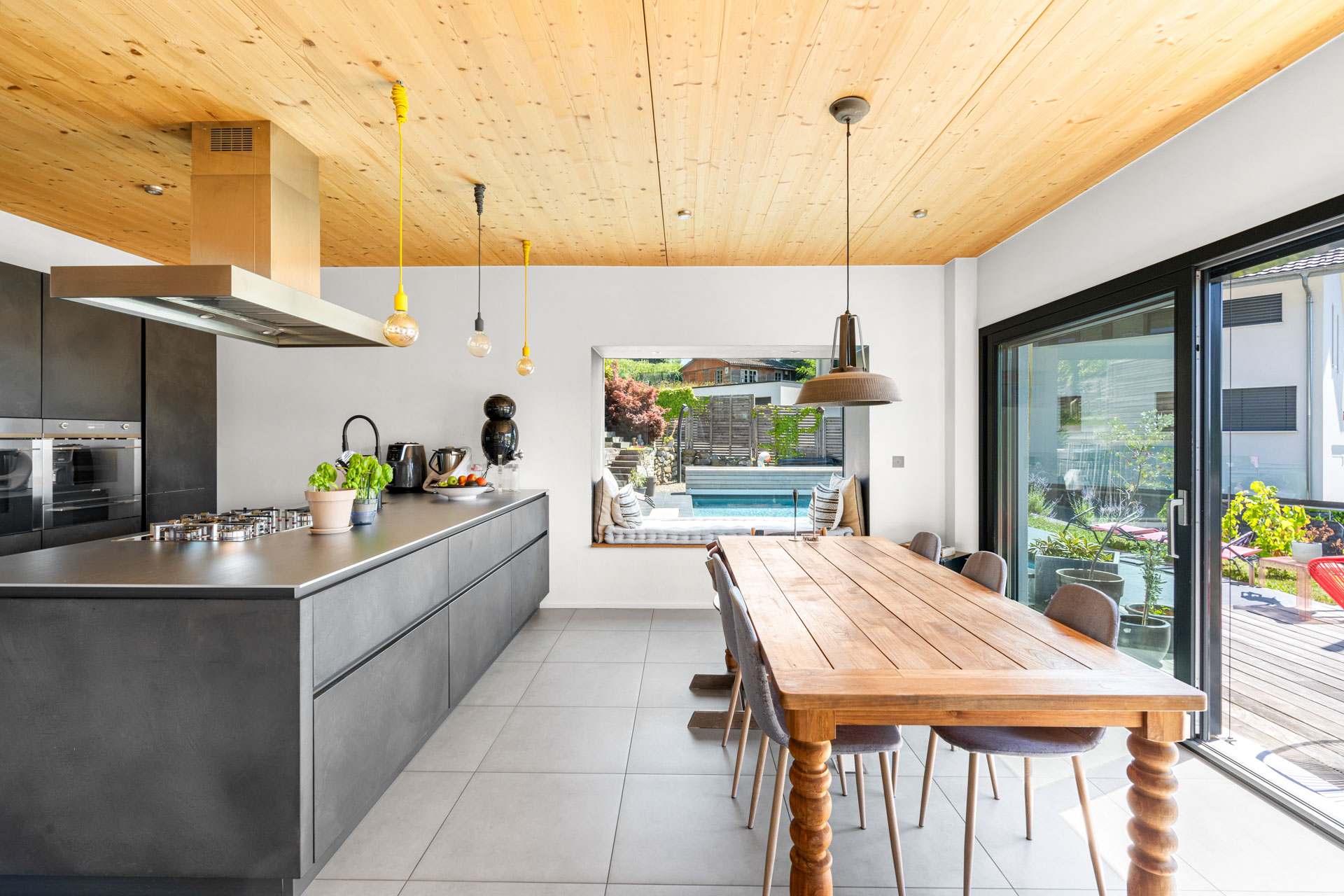 Coin salle à manger avec grande table en bois massif et vue sur la piscine extérieure à St-Légier
