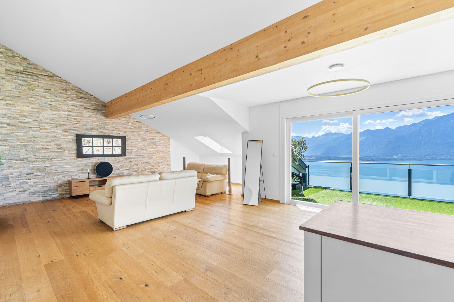 Séjour spacieux avec accès direct à une terrasse vue lac, parquet et mur en pierre à Chernex