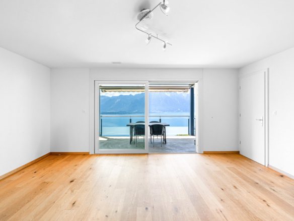 Pièce vide avec parquet et baie vitrée ouvrant sur une terrasse avec vue lac à Chernex
