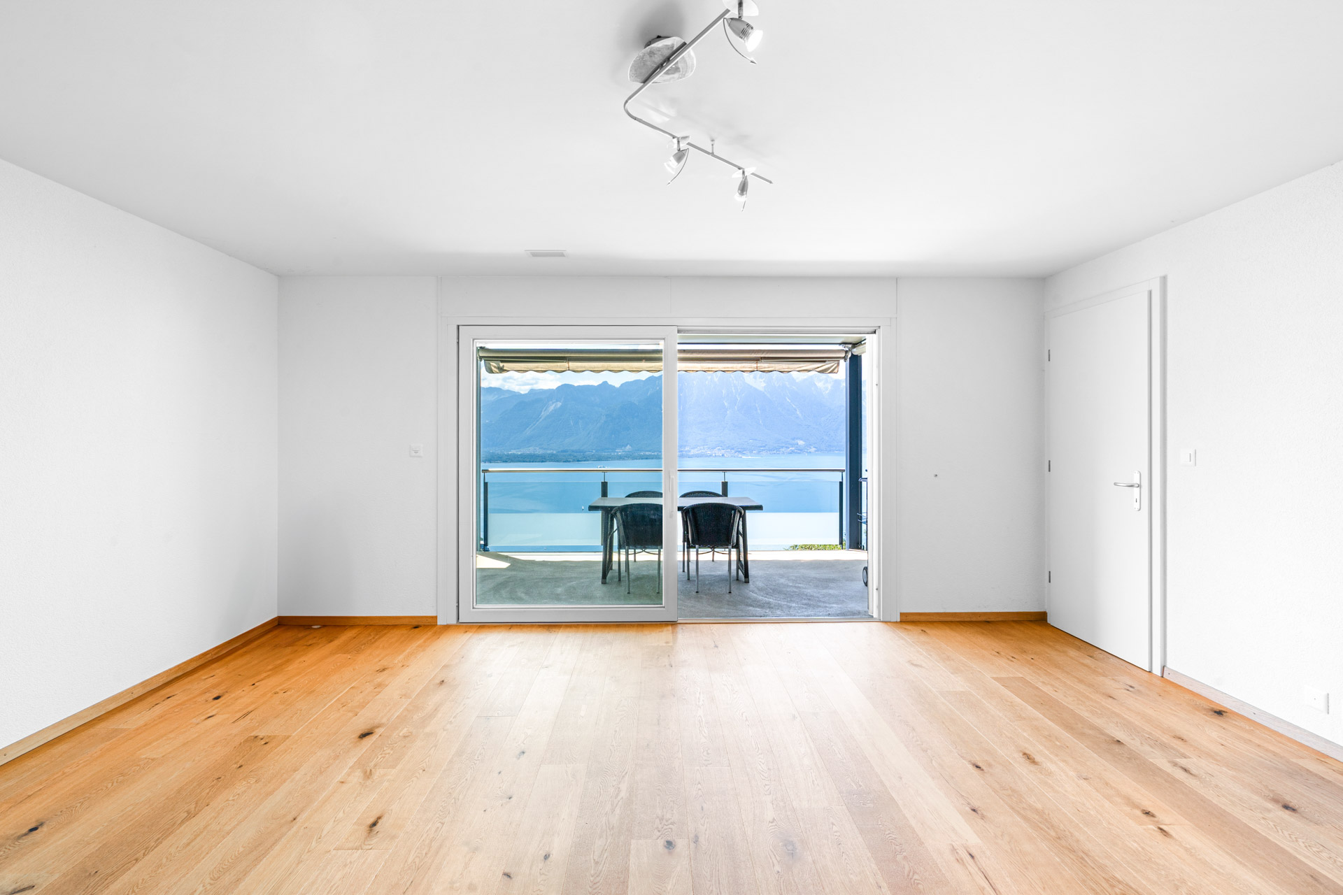 Pièce vide avec parquet et baie vitrée ouvrant sur une terrasse avec vue lac à Chernex
