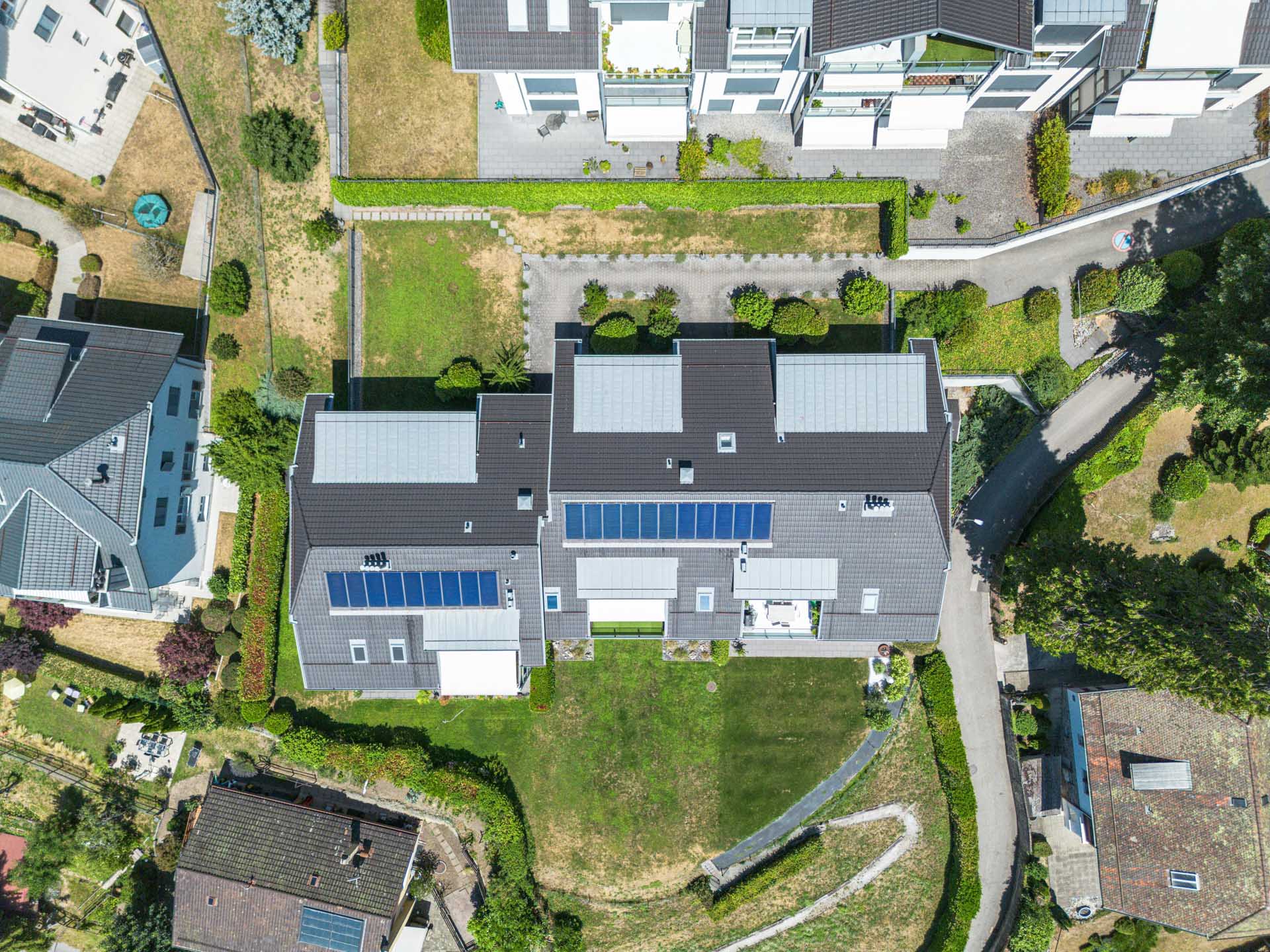 Vue aérienne verticale d’un immeuble contemporain avec toitures solaires et jardin à Chernex