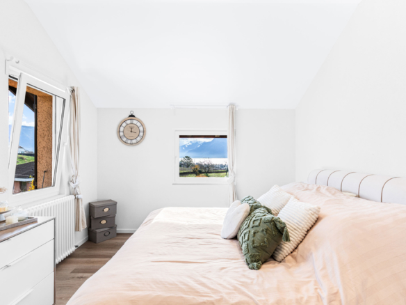 Chambre double décorée avec sobriété, grands coussins sur un lit en teinte beige et vue verdoyante.