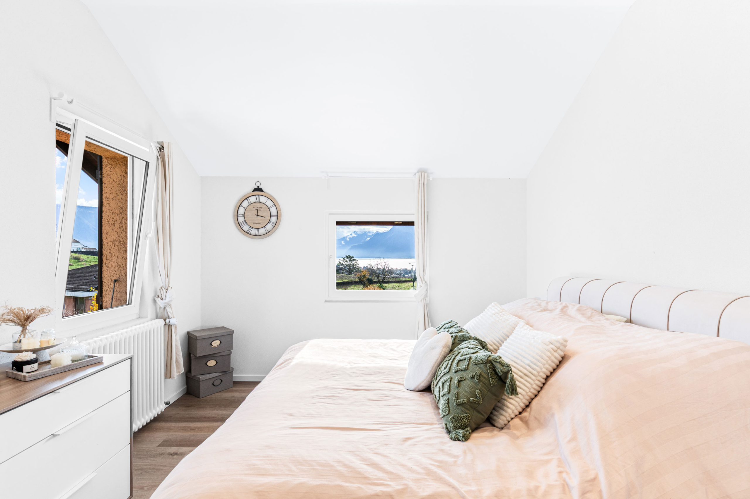 Chambre double décorée avec sobriété, grands coussins sur un lit en teinte beige et vue verdoyante.