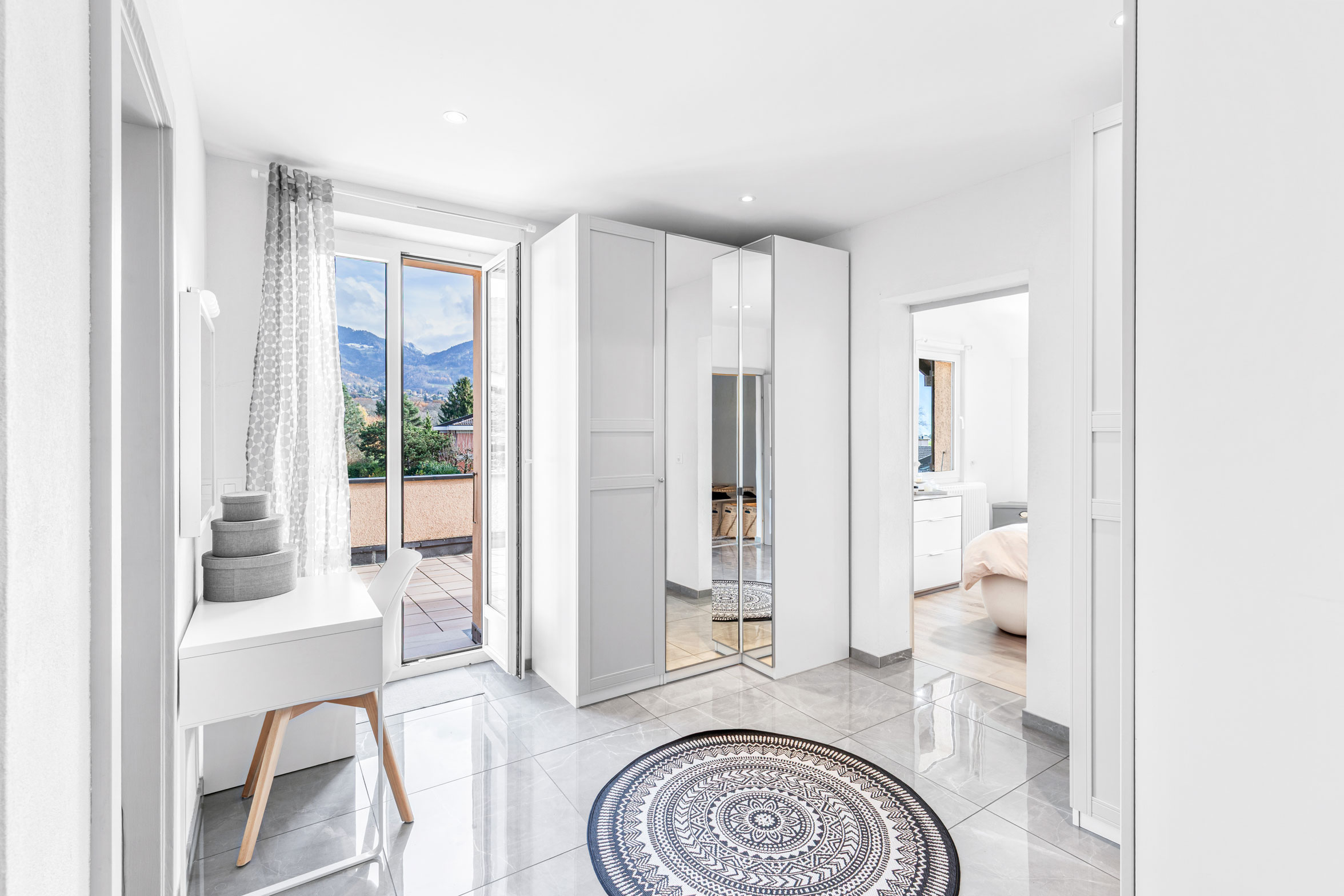Hall d’entrée lumineux avec grands rangements et accès à une terrasse extérieure avec vue montagne.