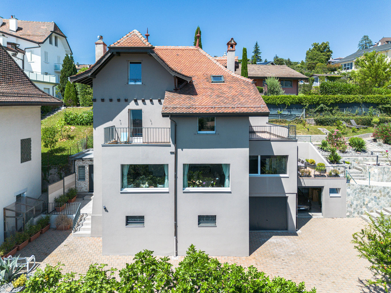 Façade arrière de la maison avec murs clairs, grandes fenêtres, terrasses et cour pavée.