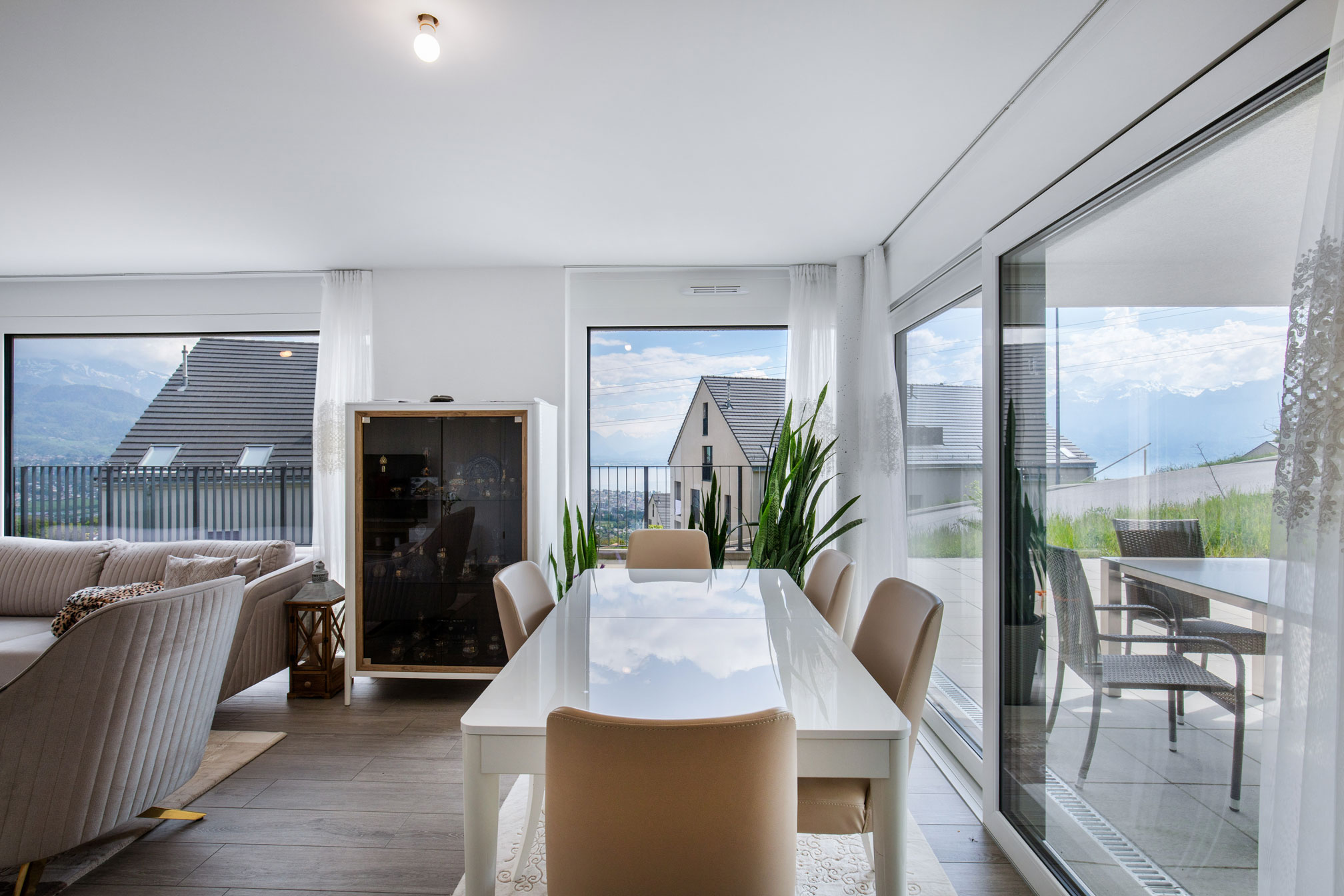 Salle à manger élégante avec mobilier blanc et grandes fenêtres offrant une vue dégagée sur les environs de Jongny.