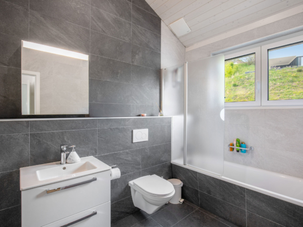 Salle de bain équipée d’une baignoire, WC suspendu et meuble vasque moderne dans une villa à Jongny.