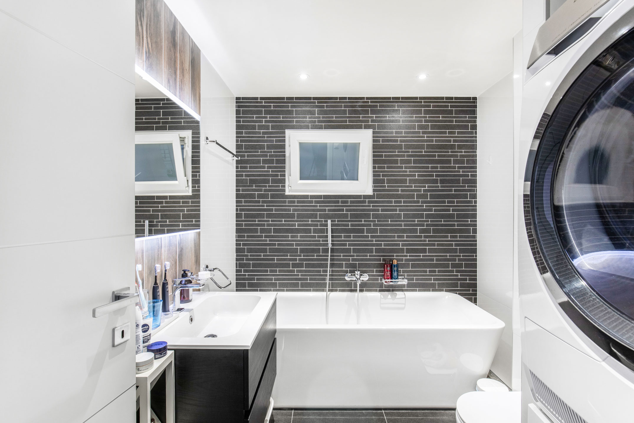Salle de bain à Chardonne avec baignoire, carrelage noir et espace buanderie