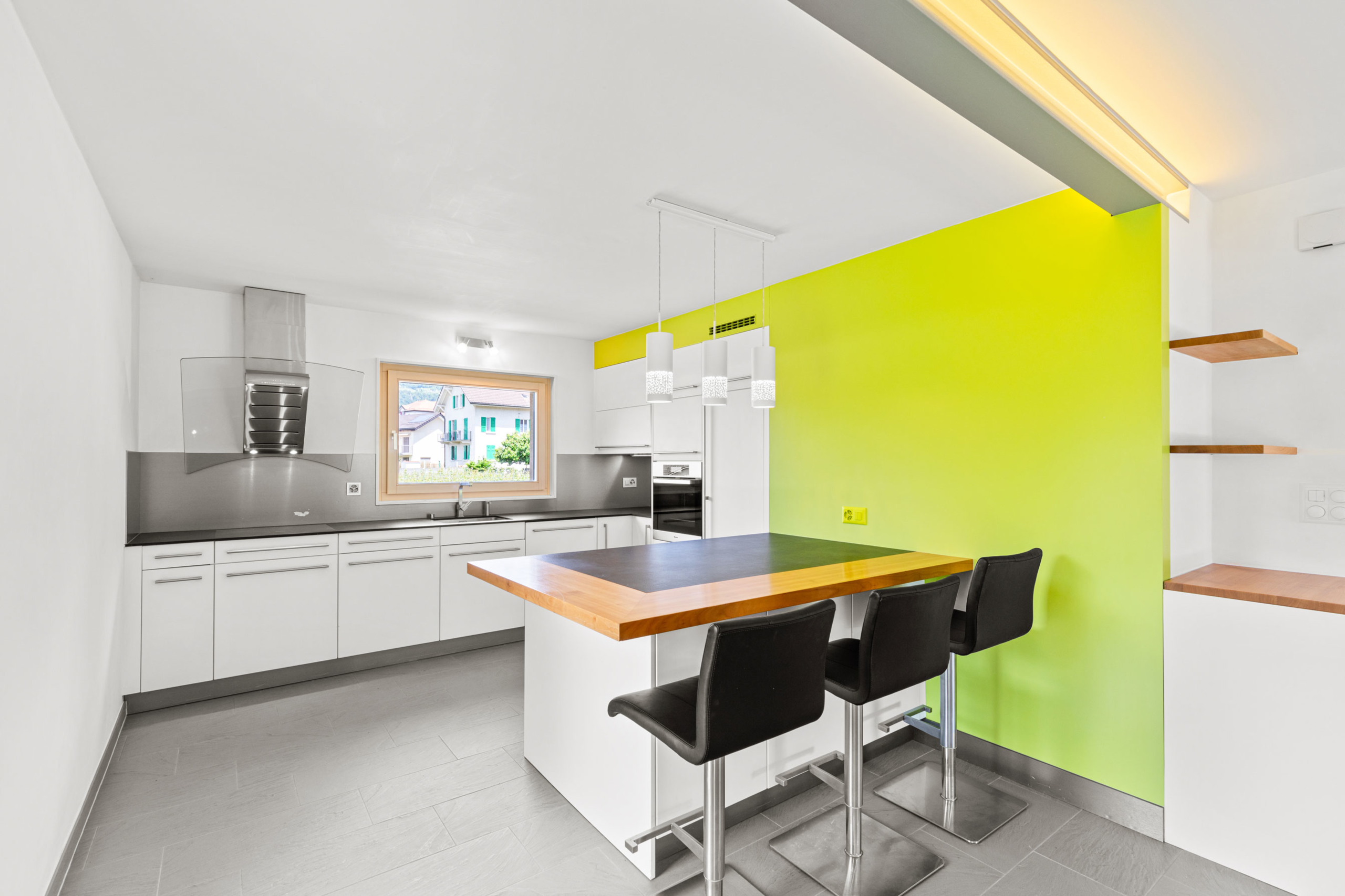 Cuisine moderne avec îlot central en bois, mur accent vert et électroménager encastré