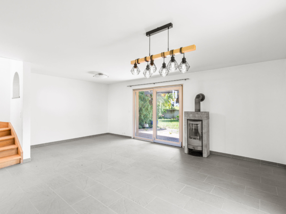 Grand séjour vide avec poêle et accès terrasse, carrelage gris clair