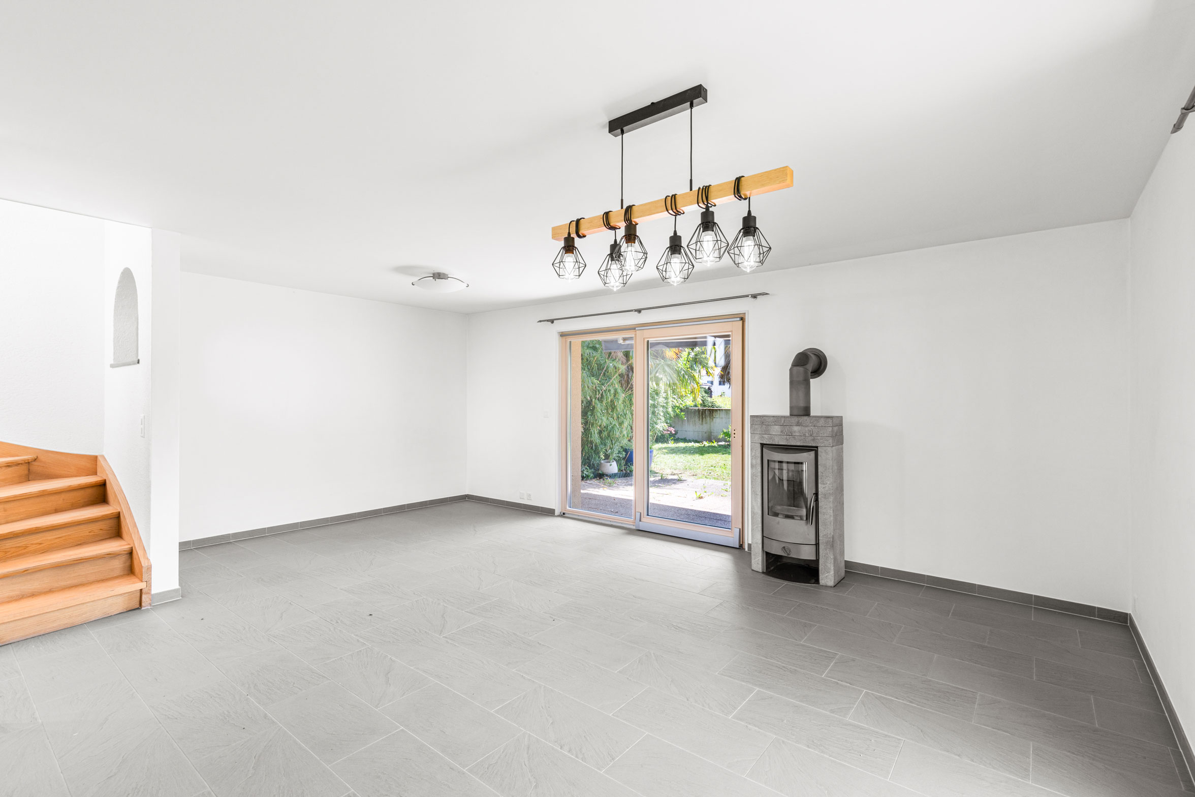Grand séjour vide avec poêle et accès terrasse, carrelage gris clair