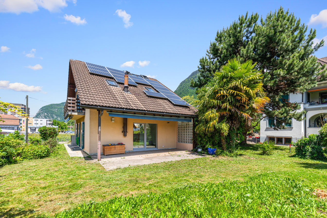 Maison individuelle avec panneaux solaires, toit en pente et jardin verdoyant