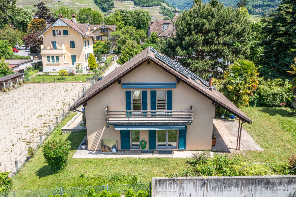 Façade arrière d’une maison avec volets bleus, balcon en bois et jardin