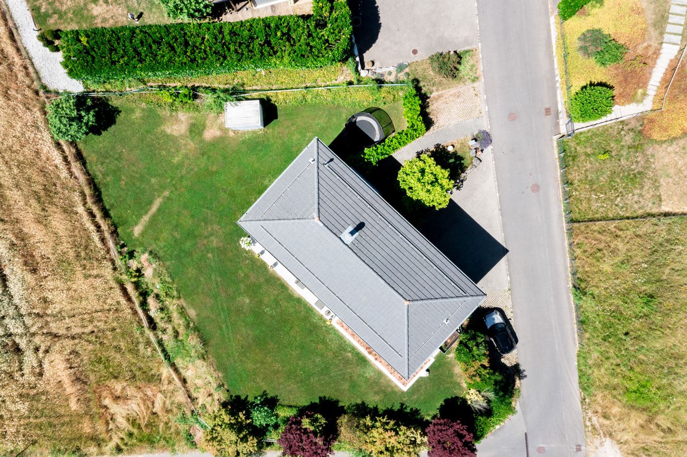 Vue aérienne verticale d'une maison moderne avec grand jardin privatif et allée de stationnement, située dans un quartier résidentiel calme.
