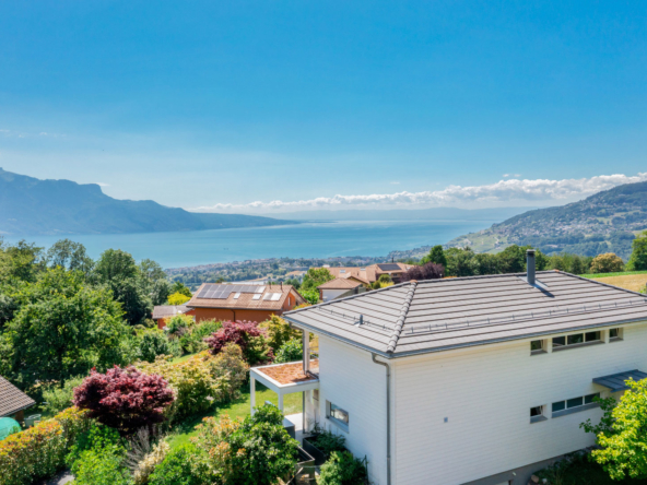 Vue latérale d’une maison surplombant le lac Léman, avec vue panoramique sur les montagnes et les toits des maisons environnantes.
