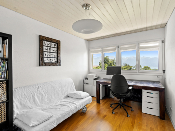 Bureau lumineux avec vue sur les montagnes, aménagé dans une pièce mansardée avec parquet et mobilier fonctionnel.