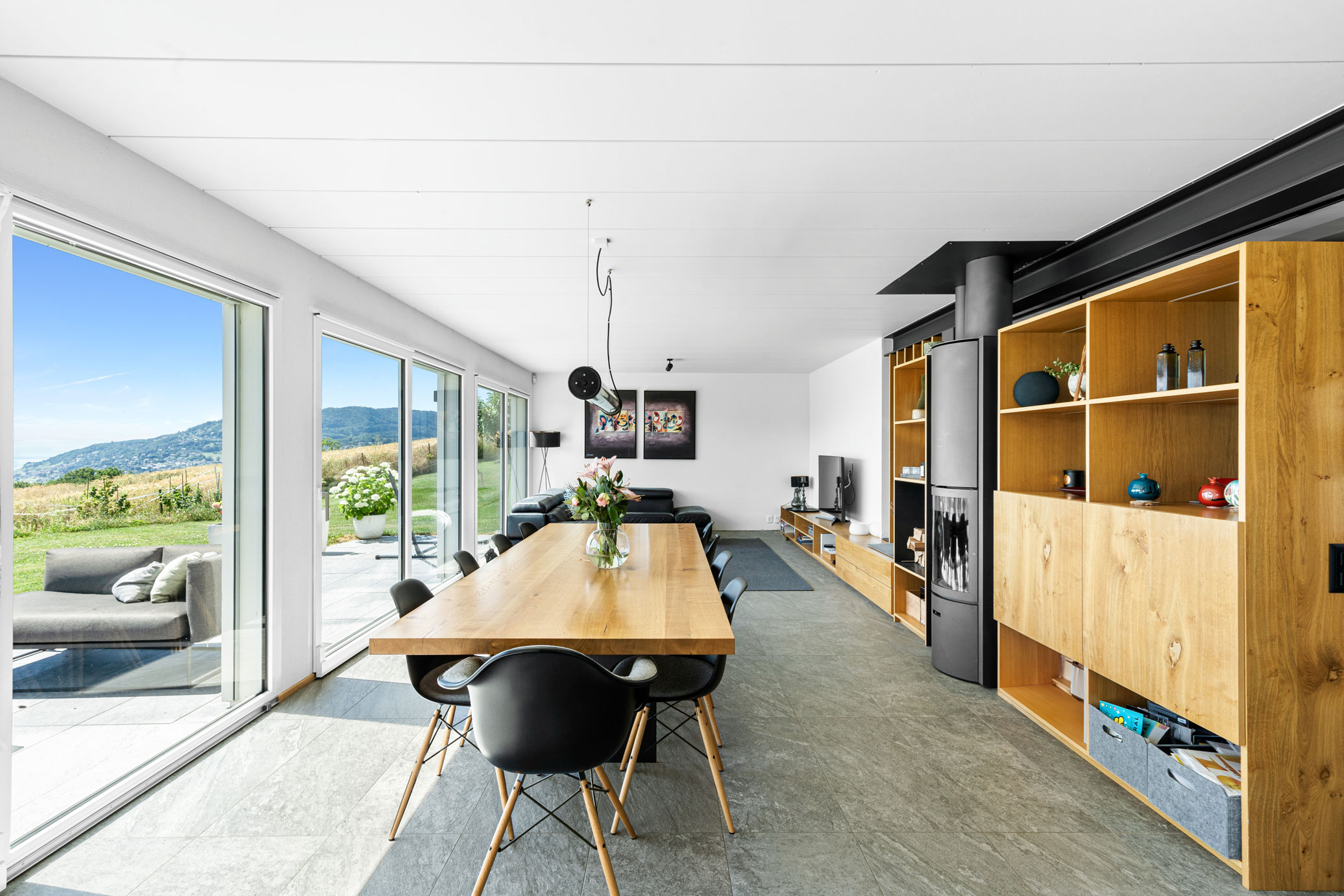 Salle à manger moderne avec grandes baies vitrées donnant sur la terrasse et le jardin, décorée dans un style épuré.