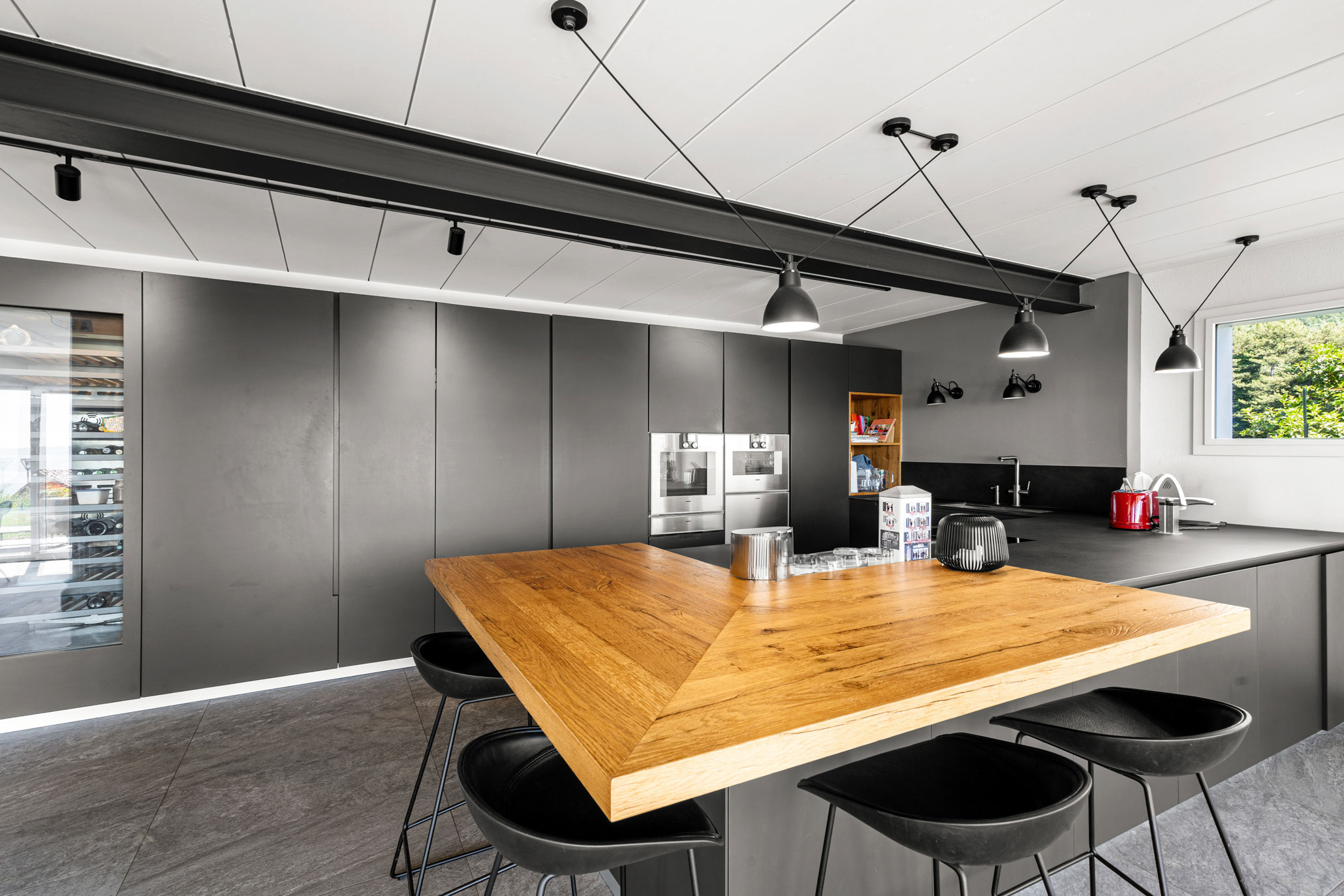 Cuisine ouverte contemporaine avec ilot central en bois massif, électroménager intégré et mobilier noir mat.