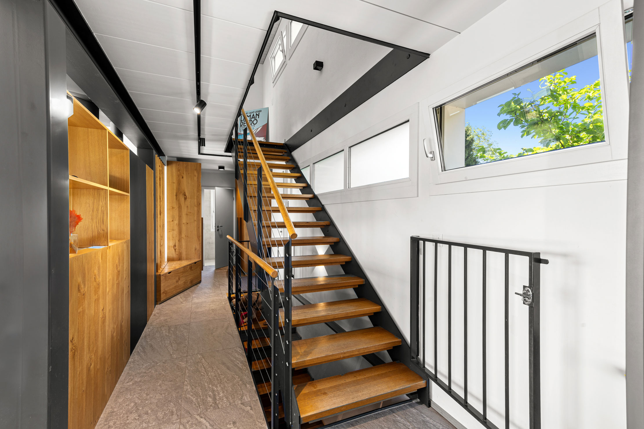 Escalier intérieur moderne en bois et métal, dans un couloir lumineux avec rangements intégrés.