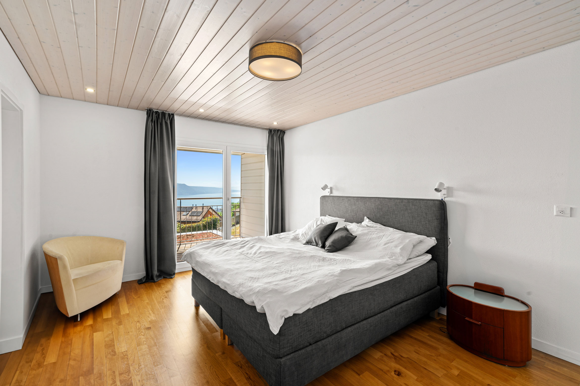 Chambre parentale avec lit double, parquet, plafond en bois et accès direct à un balcon avec vue lac.