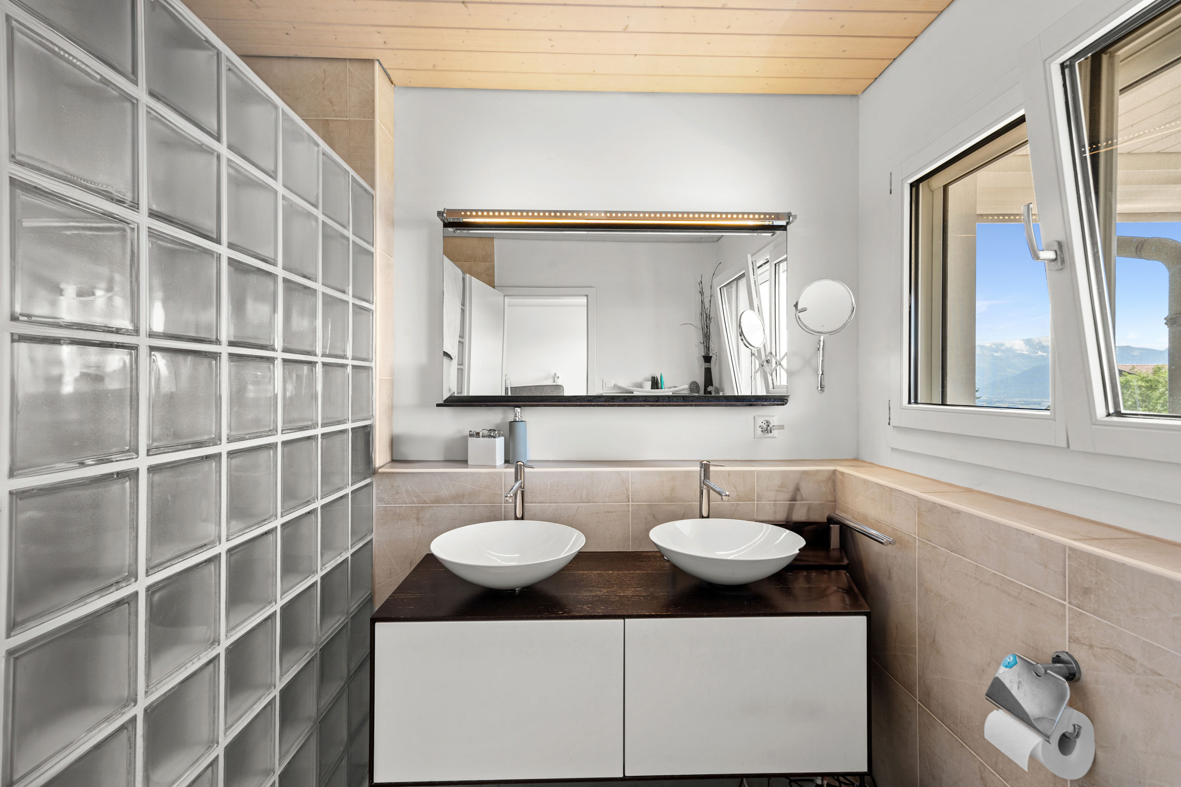 Salle de bain contemporaine avec double vasque, paroi en briques de verre et fenêtres avec vue sur le lac.