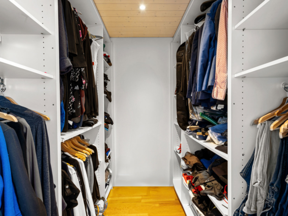 Dressing aménagé avec rangements sur mesure, éclairé par un spot au plafond et équipé de penderies et étagères.