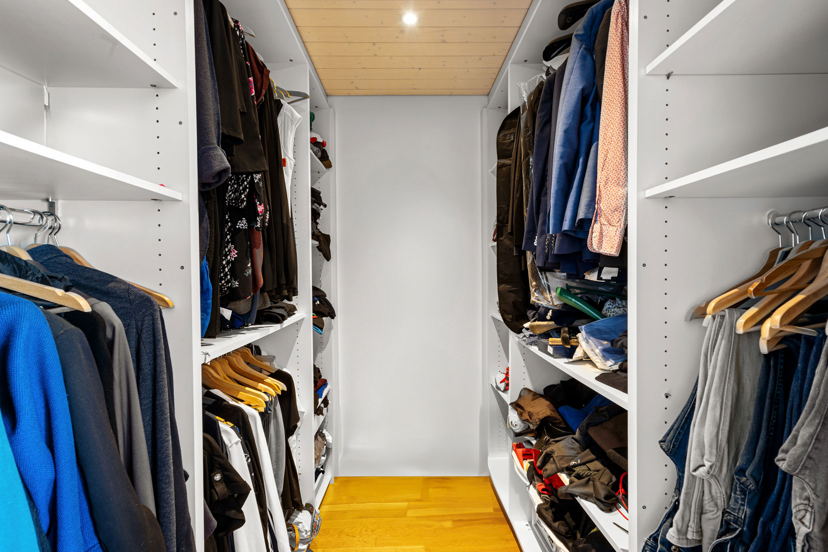 Dressing aménagé avec rangements sur mesure, éclairé par un spot au plafond et équipé de penderies et étagères.