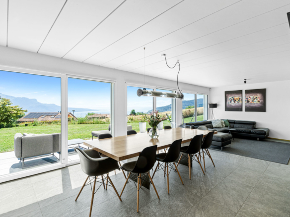 Salle à manger et salon avec grande baie vitrée, vue dégagée sur jardin et lac, mobilier moderne.