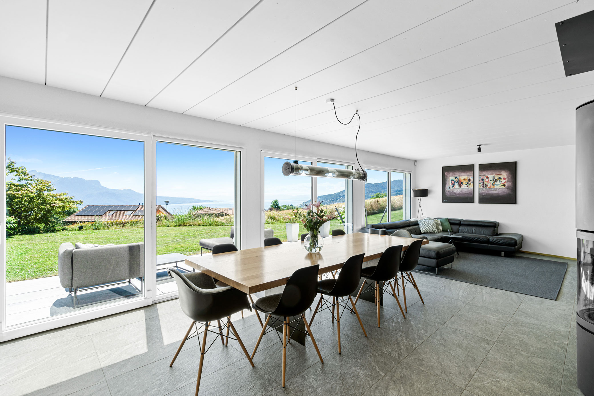 Salle à manger et salon avec grande baie vitrée, vue dégagée sur jardin et lac, mobilier moderne.