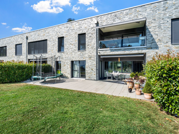 Façade en pierre d’une habitation contemporaine avec grande terrasse dallée et coin repas extérieur