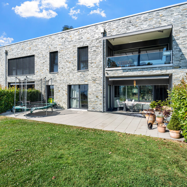 Façade en pierre d’une habitation contemporaine avec grande terrasse dallée et coin repas extérieur