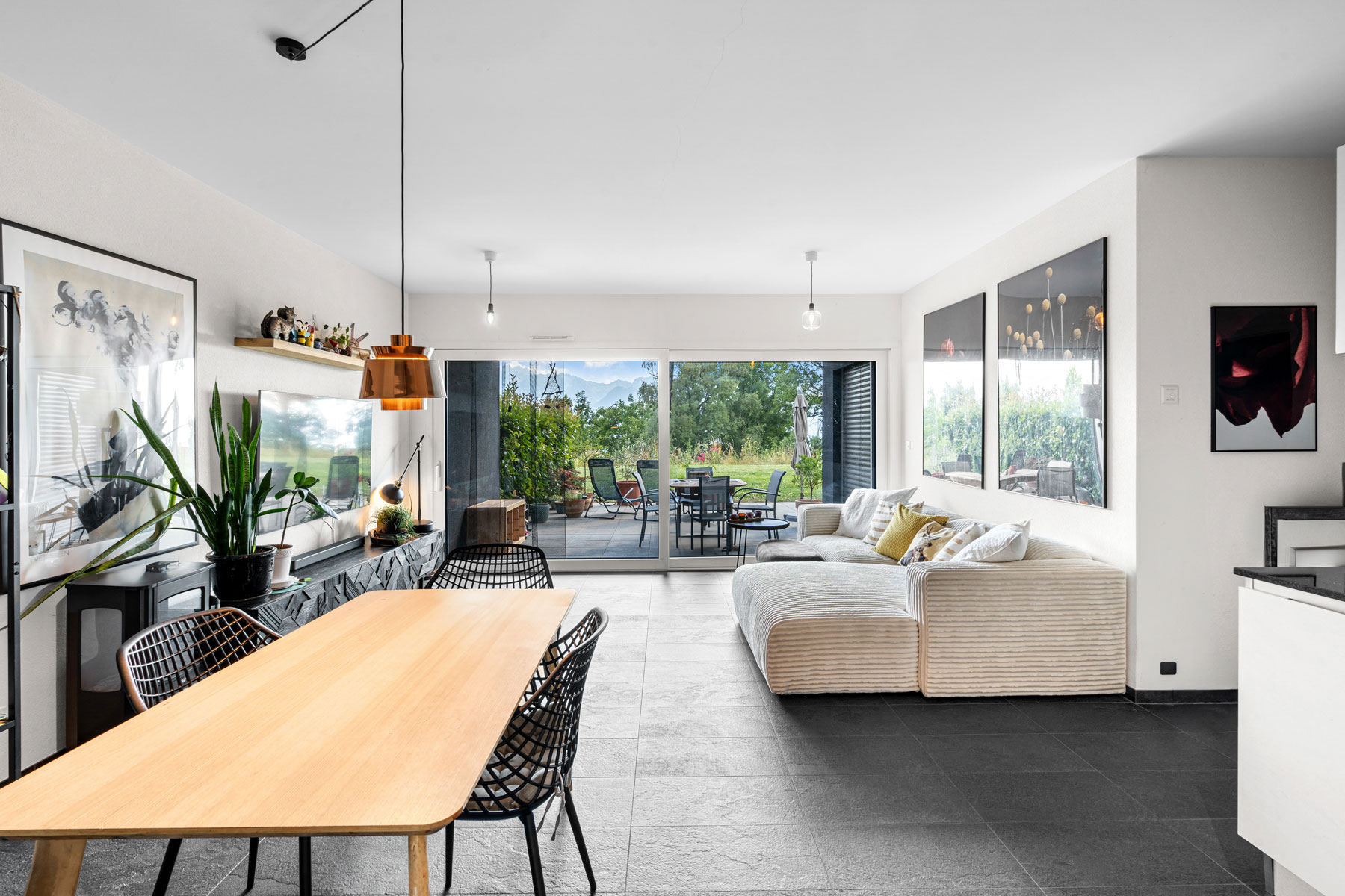 Séjour lumineux avec canapé d’angle, salle à manger et grande baie vitrée sur terrasse