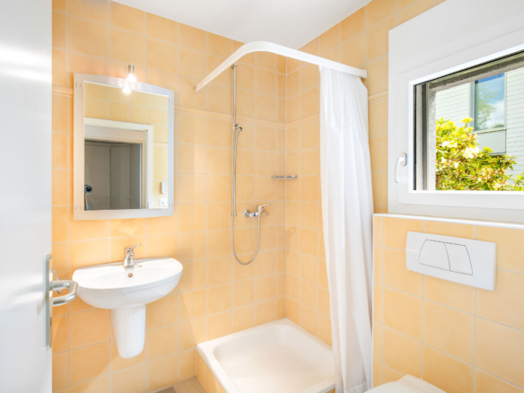Salle d’eau avec douche, carrelage jaune pastel et fenêtre donnant sur le jardin.