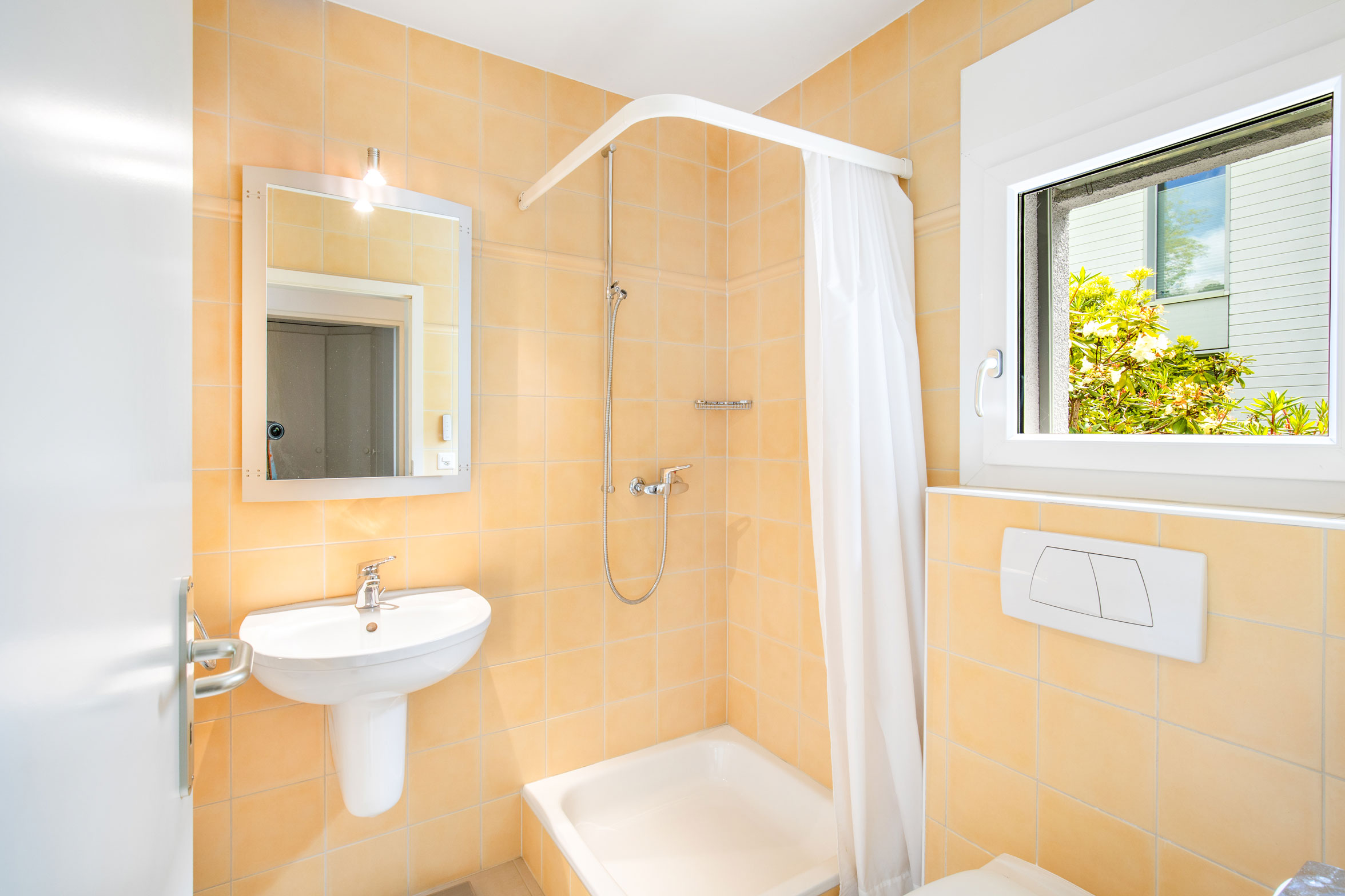 Salle d’eau avec douche, carrelage jaune pastel et fenêtre donnant sur le jardin.