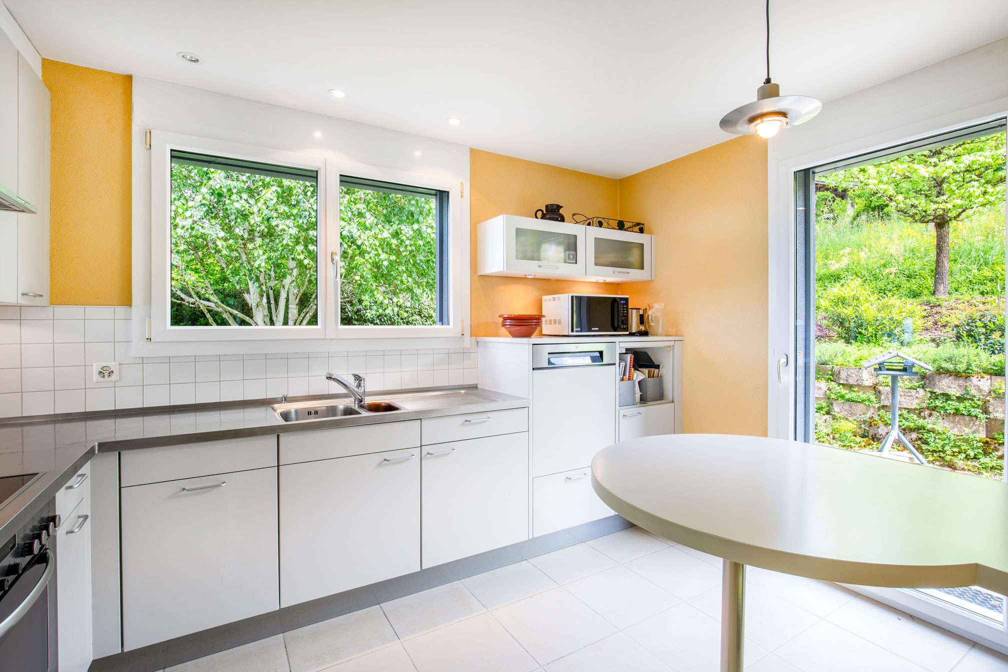 Cuisine avec mobilier blanc et sortie directe sur jardin, murs peints en jaune clair.