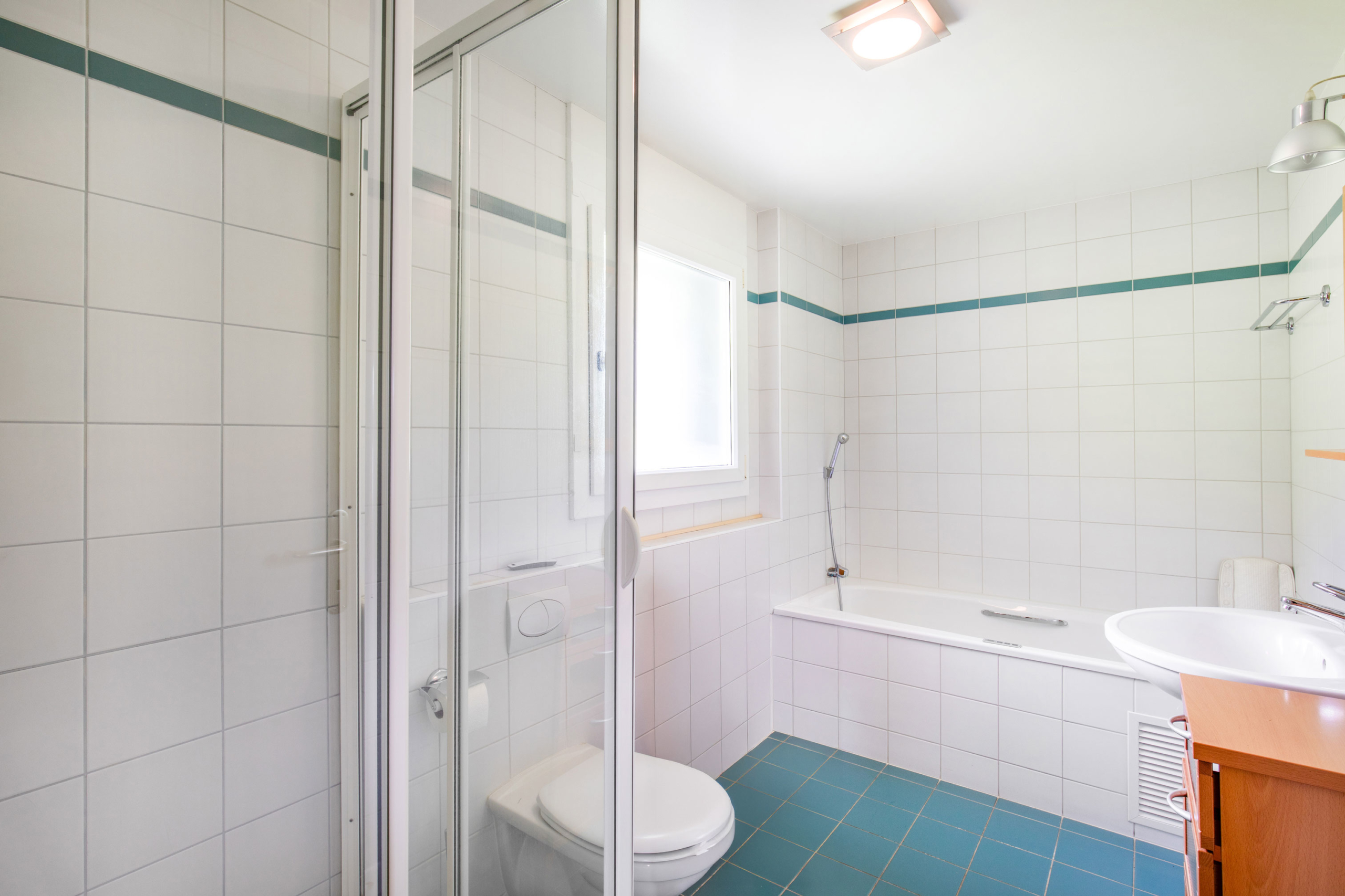 Salle de bain avec douche et baignoire, faïence blanche et sol en carrelage bleu.