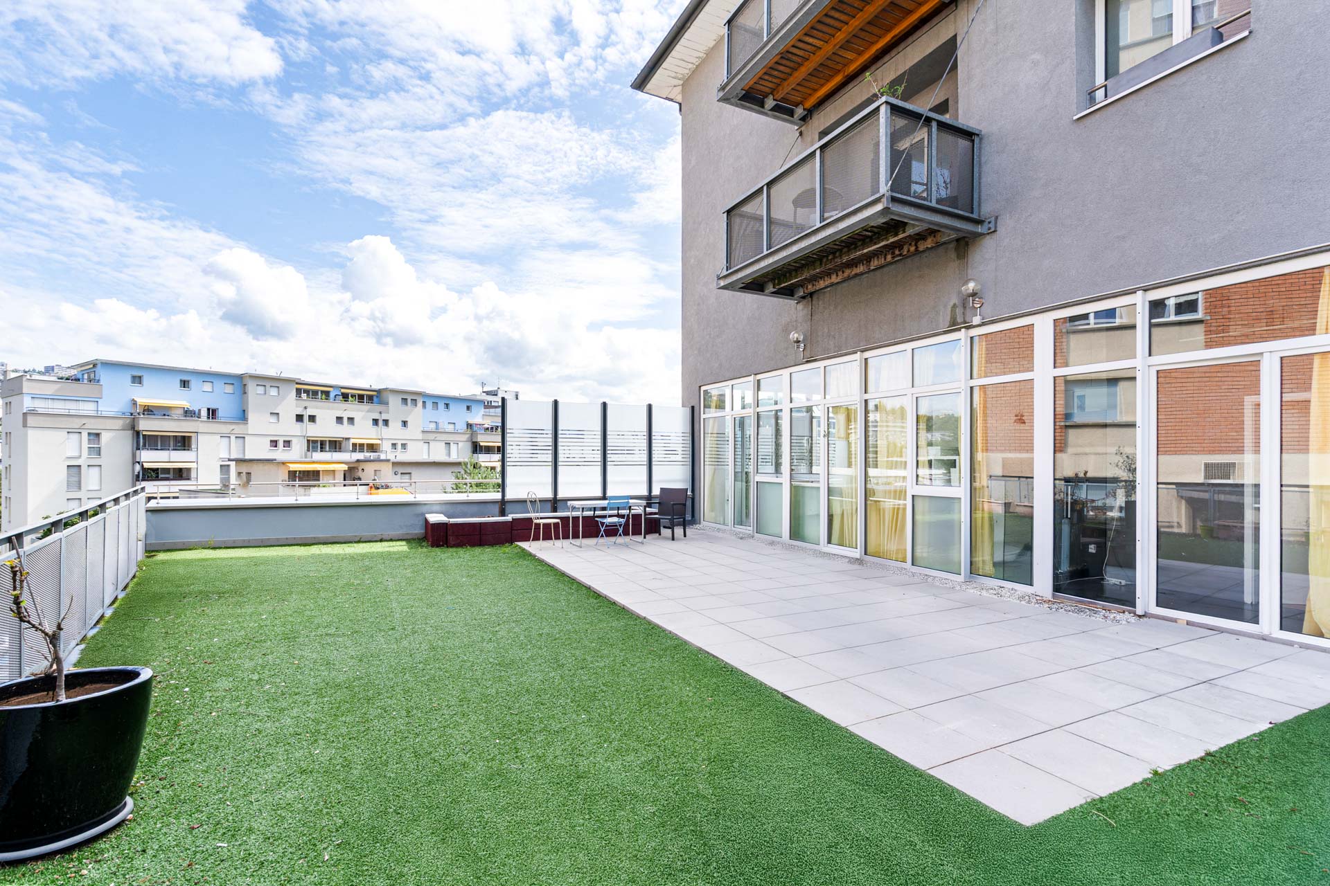 Terrasse ensoleillée attenante au salon avec sol en dalles et gazon synthétique